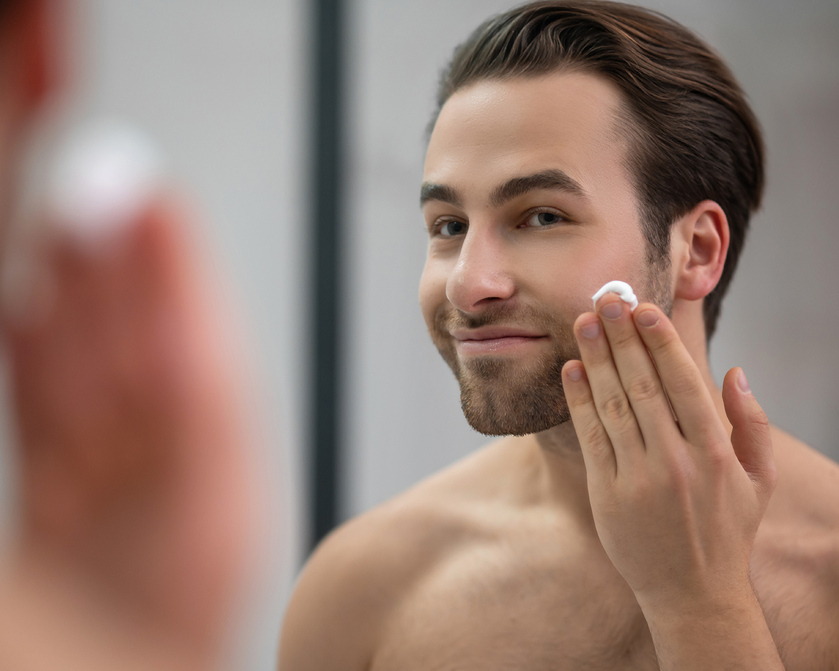 Un uomo sta davanti a uno specchio e applica il siero viso e barba sul viso.